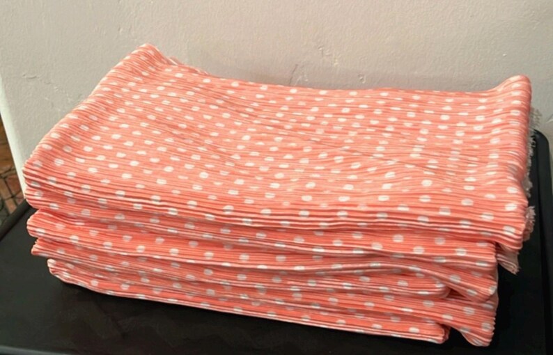 May include: A stack of four coral pink fabric napkins with white polka dots. The napkins are folded and have a pleated texture.