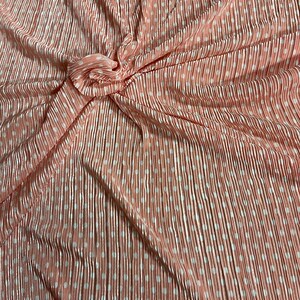 May include: Peach-colored pleated fabric with white polka dots. The fabric is wrinkled and folded.