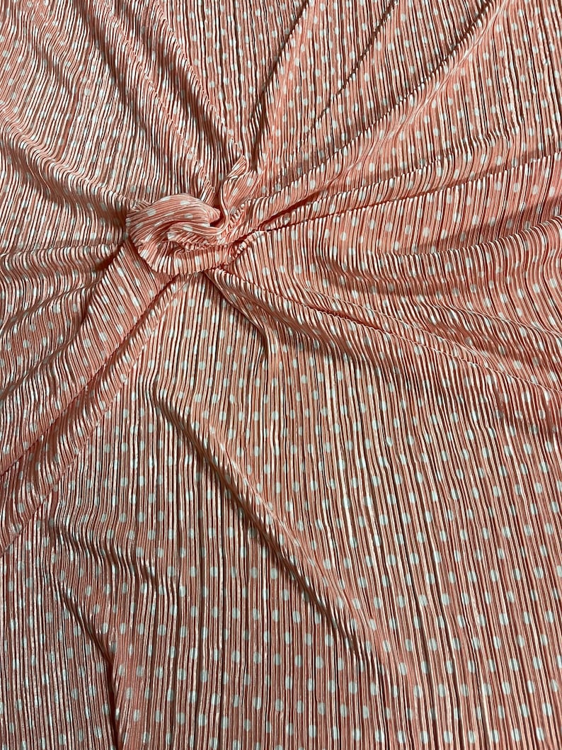 May include: Peach-colored pleated fabric with white polka dots. The fabric is wrinkled and folded.