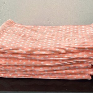 May include: A stack of peach-colored fabric with white polka dots. The fabric is pleated and has a soft, silky texture.