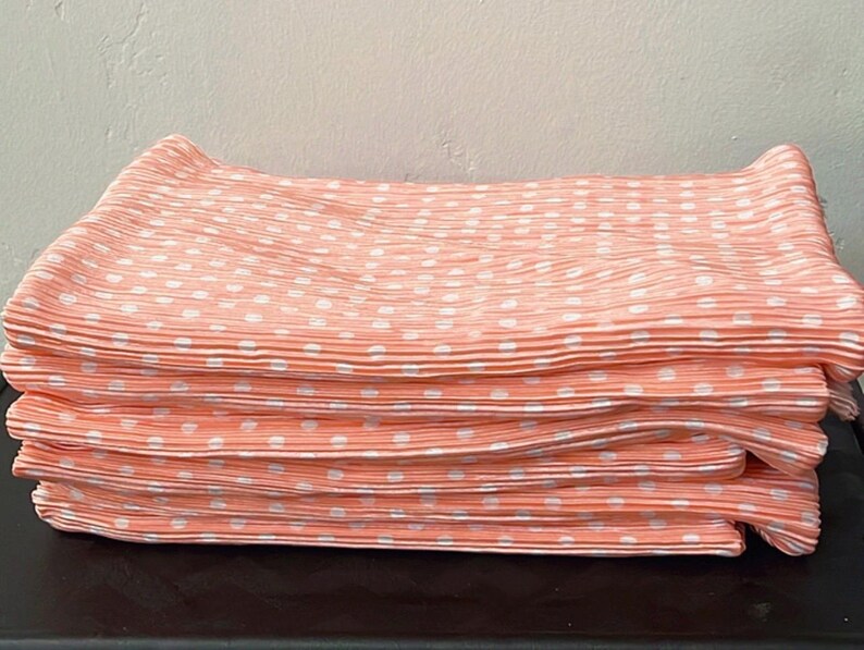 May include: A stack of peach-colored fabric with white polka dots. The fabric is pleated and has a soft, silky texture.