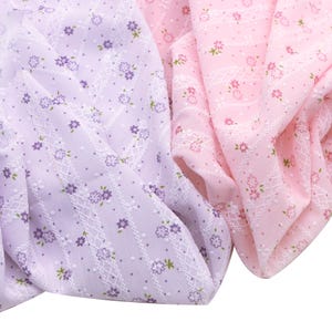 May include: Close-up of two fabrics, one lavender and one pink, both with a floral pattern. The lavender fabric has small purple flowers and a white lattice design. The pink fabric features small white flowers and a dotted pattern.