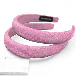 May include: Two pink padded headbands with a textured, dotted pattern. One headband is positioned above the other. A small black tag with the words "HAND MADE" is visible on one headband.