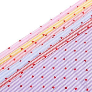 May include: A collection of fabric strips featuring diagonal stripes in pastel shades of pink, yellow, light blue, and lavender. Each strip is decorated with a repeating pattern of small, solid red hearts evenly spaced across the surface.