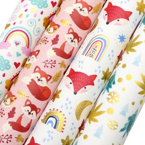 May include: Three rolls of wrapping paper with different designs. The first roll features a rainbow, hearts, and clouds on a white background. The second roll features foxes and leaves on a pink background. The third roll features a rainbow, stars, and snowflakes on a white background.