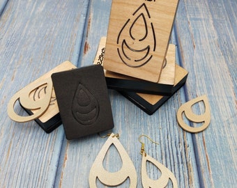 May include: Two pairs of gold leather earrings with a teardrop shape and a double-layered design. The earrings are displayed next to two wooden cutting dies with the same teardrop shape. The dies are labeled "2 inch".