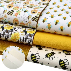 May include: Five sheets of patterned faux leather featuring a bee theme. The sheets are stacked on top of each other and include a yellow sheet, a white sheet with black bees, a white sheet with yellow bees and flowers, a white sheet with black bees and honeycomb, and a gold glitter sheet.