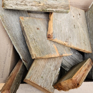 May include: A collection of weathered, rectangular wooden planks in varying sizes and shades of gray and brown. Some planks show visible grain and nail holes, suggesting reclaimed or rustic wood. The planks are arranged inside a cardboard box.