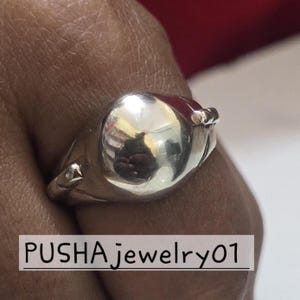 Puede incluir: Un anillo de plata con un centro grande, redondo, liso y pulido. El anillo tiene un diseño decorativo en la banda.