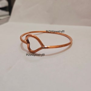 May include: A copper heart-shaped bangle bracelet. The bracelet is simple and elegant, with a smooth finish.  PUSHAJewelry01 is printed on the bracelet.