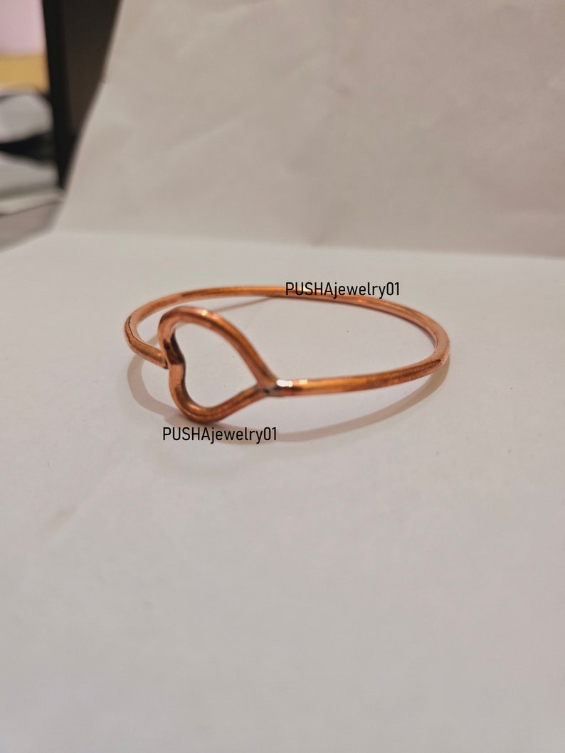 May include: A copper heart-shaped bangle bracelet. The bracelet is simple and elegant, with a smooth finish.  PUSHAJewelry01 is printed on the bracelet.