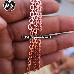 May include: A close-up of a copper chain necklace. The chain is made of small, linked circles. The chain is held in a hand, and the text "PUSHAjewelry01" is visible in the background.
