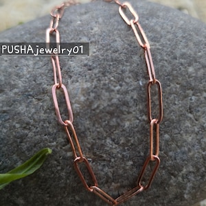 Puede incluir: Un collar de cadena de cobre con un diseño simple y enlazado. La cadena está hecha de pequeños eslabones rectangulares.