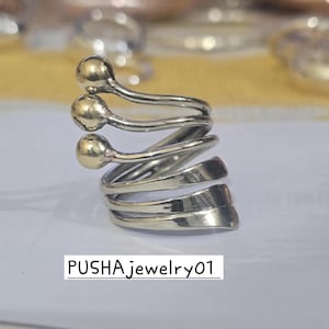 May include: A silver ring with three gold balls on the top. The ring is made of twisted metal and has a unique design.