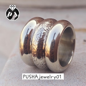 May include: A silver ring with three connected bands. The center band features an engraved floral pattern, while the outer bands are smooth and polished. The text "PUSHA jewelry01" is at the bottom.