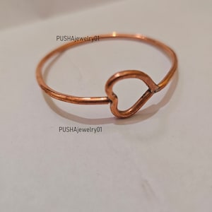 May include: A simple copper ring with a heart-shaped cutout. The ring is on a white surface.  PUSHAjewelry01 is written on the surface.