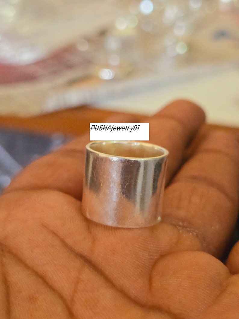 May include: A silver ring with a smooth, polished finish. The ring is thick and wide, with a simple, modern design.