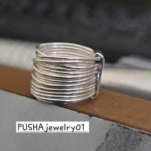 May include: A silver ring featuring multiple bands stacked on top of each other. The ring is crafted from thin, round wire that is twisted and woven together. The ring is a statement piece and would be a great addition to any jewellery collection.