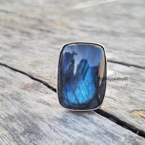 Peut inclure: Une bague en argent avec une grande pierre rectangulaire en labradorite bleue. La pierre a un effet chatoyant et irisé.