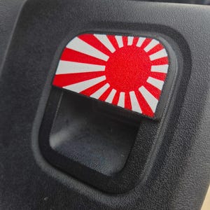 May include: A red and white rising sun decal on a black car door handle.