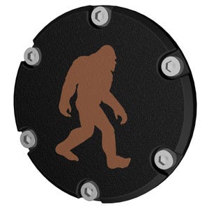 May include: Black round motorcycle cover with six silver bolts and a brown silhouette of Bigfoot walking.