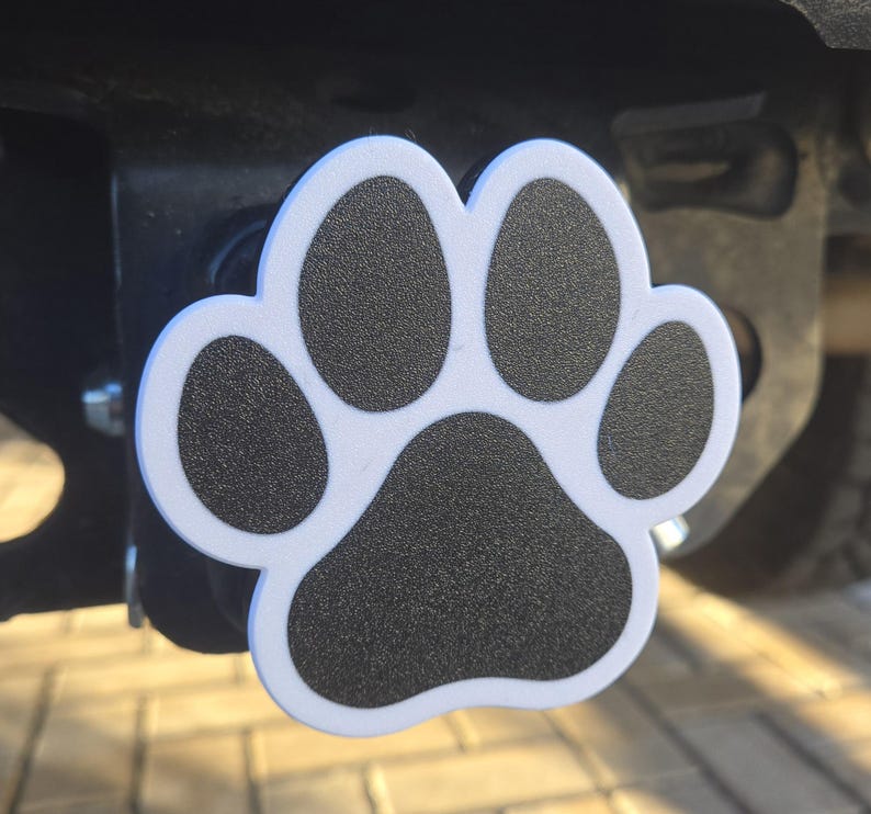 May include: White plastic paw print hitch cover with black detailing. The paw print is a popular design for pet lovers.