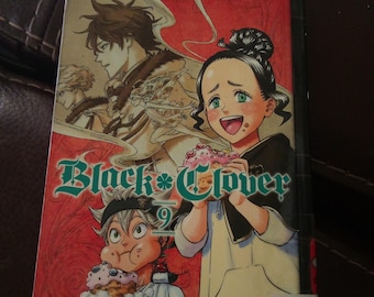 Puede incluir: Manga "Black Clover" volumen 9. La portada presenta ilustraciones de anime coloridas de personajes, incluyendo una joven con ojos verdes y un chico con una cinta en la cabeza. El título está en letras grandes y verdes.