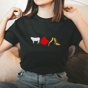 May include: A black t-shirt with a white bull, red cape, blonde braid, and a gold high heel shoe graphic.