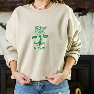May include: A beige sweatshirt with a green graphic of a plant with the text "FEED ME!" printed on the front.