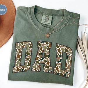 Cool and rugged Camo Dad Shirt designed for the ultimate Hunting Dad—perfect as a New Dad Father's Day Gift or Dad Birthday Gift. This comfortable and stylish Camouflage Dad Shirt makes a great Gift for Dad who loves the outdoors. A must-have Dad Tee for everyday wear, this Dad Tshirt is a top pick for any proud papa. Whether you're shopping for a Dad Gift or the Best Dad Gift, this shirt delivers both style and sentiment.