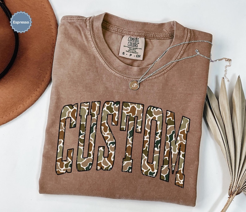 Custom Camo Shirt featuring bold varsity-style font — the perfect Camouflage Shirt for deer hunting, duck hunting, or casual wear during hunting season. This cozy Camo Sweatshirt makes a thoughtful Hunting Lover Gift, combining rugged outdoor style with personalized comfort.