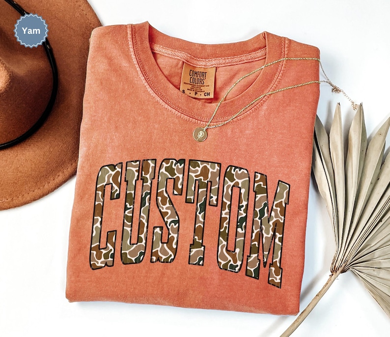 Custom Camo Shirt featuring bold varsity-style font — the perfect Camouflage Shirt for deer hunting, duck hunting, or casual wear during hunting season. This cozy Camo Sweatshirt makes a thoughtful Hunting Lover Gift, combining rugged outdoor style with personalized comfort.