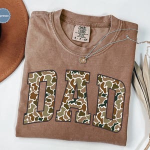 Cool and rugged Camo Dad Shirt designed for the ultimate Hunting Dad—perfect as a New Dad Father's Day Gift or Dad Birthday Gift. This comfortable and stylish Camouflage Dad Shirt makes a great Gift for Dad who loves the outdoors. A must-have Dad Tee for everyday wear, this Dad Tshirt is a top pick for any proud papa. Whether you're shopping for a Dad Gift or the Best Dad Gift, this shirt delivers both style and sentiment.