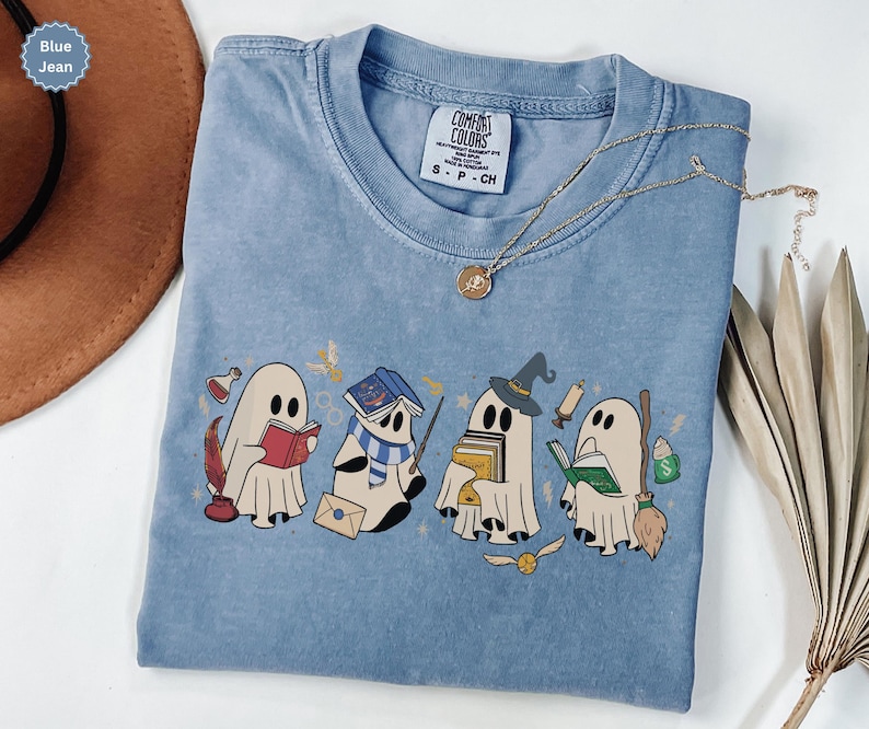 Halloween ghost shirt featuring four cute reading ghosts dressed as magical wizard characters with books, broomstick, owl, potion, and spooky season graphics on a cozy Halloween graphic tee.
