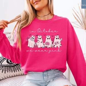 Pink Ghost Nurse Shirt featuring adorable ghost nurses with pink nurse stethoscopes and nurse items, with the phrase "In October We Wear Pink" in a script lettering. This Halloween Tee is perfect for healthcare heroes supporting Breast Cancer Awareness during spooky season. A thoughtful and festive Oncology Nurse Tee or Cute Nurse Tshirt for October events, hospital shifts, or awareness walks. Celebrate with this Pink Ribbon Shirt designed for nurses or medical assistants who care.