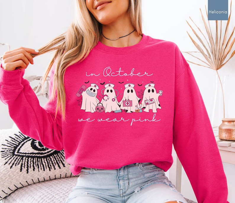 Pink Ghost Nurse Shirt featuring adorable ghost nurses with pink nurse stethoscopes and nurse items, with the phrase "In October We Wear Pink" in a script lettering. This Halloween Tee is perfect for healthcare heroes supporting Breast Cancer Awareness during spooky season. A thoughtful and festive Oncology Nurse Tee or Cute Nurse Tshirt for October events, hospital shifts, or awareness walks. Celebrate with this Pink Ribbon Shirt designed for nurses or medical assistants who care.