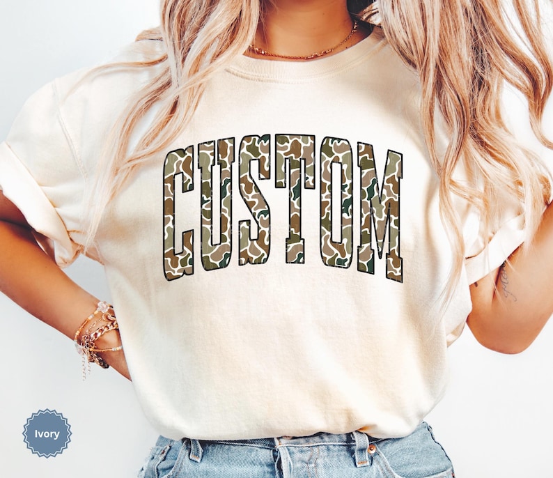 Custom Camo Shirt featuring bold varsity-style font — the perfect Camouflage Shirt for deer hunting, duck hunting, or casual wear during hunting season. This cozy Camo Sweatshirt makes a thoughtful Hunting Lover Gift, combining rugged outdoor style with personalized comfort.