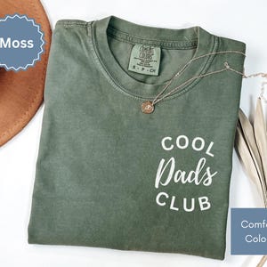 May include: A green t-shirt with the text "Cool Dad's Club" in white lettering. The shirt is made by Comfort Colors.