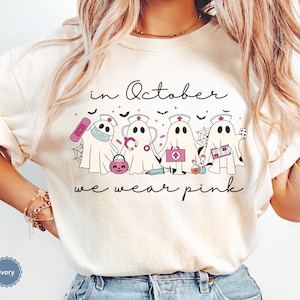Pink Ghost Nurse Shirt featuring adorable ghost nurses with pink nurse stethoscopes and nurse items, with the phrase "In October We Wear Pink" in a script lettering. This Halloween Tee is perfect for healthcare heroes supporting Breast Cancer Awareness during spooky season. A thoughtful and festive Oncology Nurse Tee or Cute Nurse Tshirt for October events, hospital shifts, or awareness walks. Celebrate with this Pink Ribbon Shirt designed for nurses or medical assistants who care.