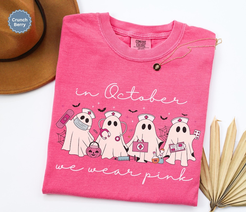 Pink Ghost Nurse Shirt featuring adorable ghost nurses with pink nurse stethoscopes and nurse items, with the phrase "In October We Wear Pink" in a script lettering. This Halloween Tee is perfect for healthcare heroes supporting Breast Cancer Awareness during spooky season. A thoughtful and festive Oncology Nurse Tee or Cute Nurse Tshirt for October events, hospital shifts, or awareness walks. Celebrate with this Pink Ribbon Shirt designed for nurses or medical assistants who care.