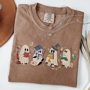Halloween ghost shirt featuring four cute reading ghosts dressed as magical wizard characters with books, broomstick, owl, potion, and spooky season graphics on a cozy Halloween graphic tee.