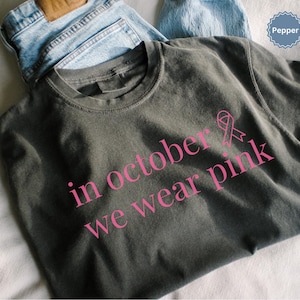 In October We Wear Pink in a simple lettering. This Halloween Tee is perfect for healthcare heroes or anyone supporting Breast Cancer Awareness during spooky season. A thoughtful and festive Oncology Nurse Tee or Cute Nurse Tshirt for October events, hospital shifts, or awareness walks. Celebrate with this Pink Ribbon Shirt designed for nurses or medical assistants who care.