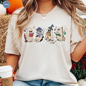 Halloween ghost shirt featuring four cute reading ghosts dressed as magical wizard characters with books, broomstick, owl, potion, and spooky season graphics on a cozy Halloween graphic tee.