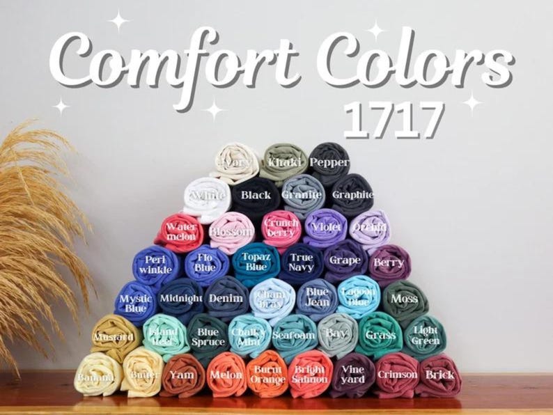 May include: A display of rolled Comfort Colors t-shirts in various colors, arranged in a pyramid shape. The image includes the text "Comfort Colors 1717" at the top. Colors include black, blue, green, pink, and yellow.