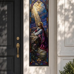 Puede incluir: Un panel de ventana de vidriera alto y rectangular que muestra una figura con cabello largo y un halo, arrodillada en oración sobre una superficie rocosa. La escena incluye rayos de luz que descienden sobre un fondo de nubes azules y moradas.