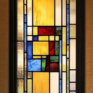 Könnte beinhalten: Ein Buntglasfenster mit einem geometrischen Muster aus gelben, blauen, roten und grünen Glasscheiben.