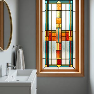 Könnte beinhalten: Ein rechteckiges Buntglasfenster mit einem geometrischen Muster aus leuchtend orangefarbenen, roten und türkisfarbenen Glassegmenten, die von dünnen schwarzen Bleilinien umrahmt sind und in einem hellen Holzrahmen sitzen.
