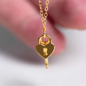 May include: A gold necklace featuring a heart-shaped padlock with a key charm. The necklace is dainty and feminine.