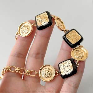 May include: Gold and black bracelet with square and round links. The links have a raised, ornate design.