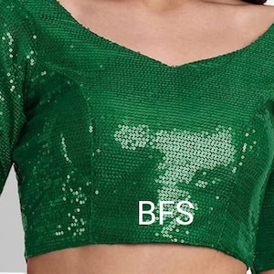Puede incluir: Un top corto verde con lentejuelas, cuello en V y mangas cortas. El top tiene las letras "BFS" impresas en la parte delantera.